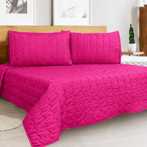 Cover acolchado Arlin color fucsia de microfibra con diseño punzonado y fundas de almohada a juego sobre cama